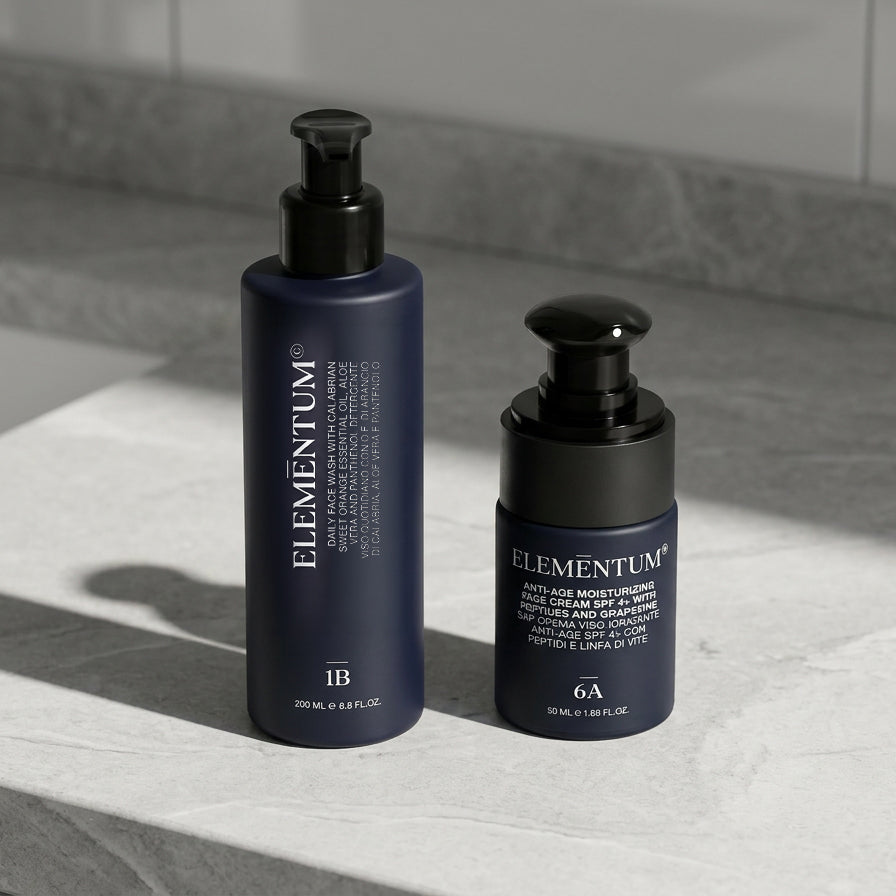 Two bottles of Elementum skincare products on a marble surface with a tiled wall background.