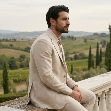 Man in a beige suit sitting on a balcony with a scenic landscape in the background