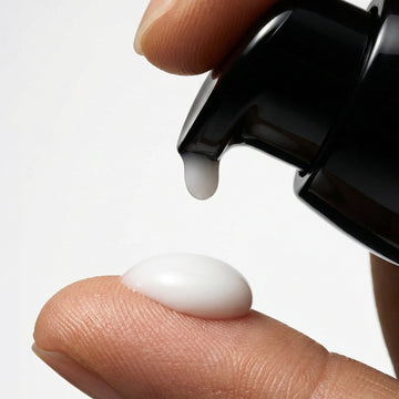 Black dropper bottle dispensing a white liquid onto a finger against a light gray background